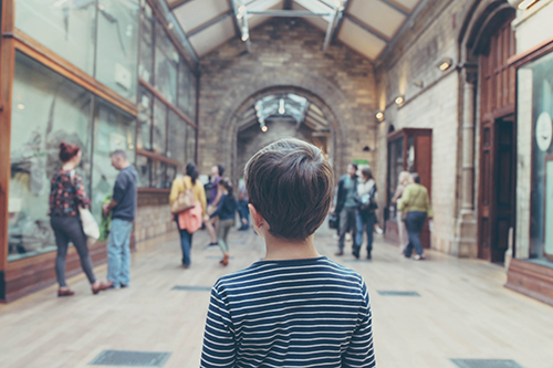 Young boy standing in an exhibition space surrounded by other guests looking at exhibitions.