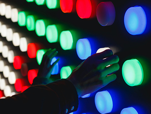 Hands pressing colourful light buttons on a wall