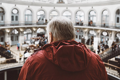 Man wearing a red coat standing on a balcony in an auditorium looking out at the guests.